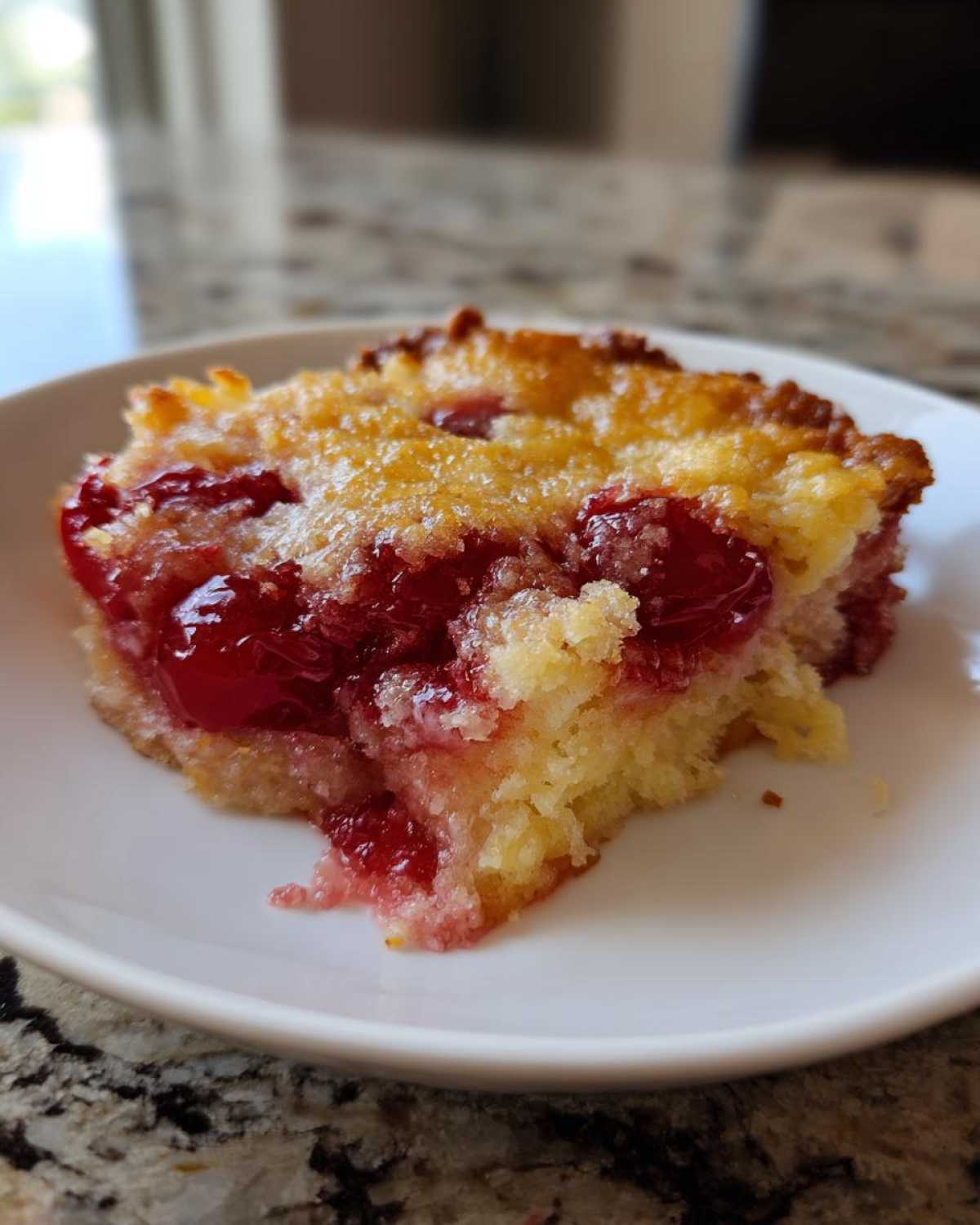 Close-up of a warm slice of cherry dump cake with a golden top and bright red cherries.