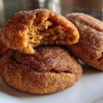 Close-up of three chewy pumpkin snickerdoodle cookies coated in cinnamon sugar, one broken open to show the soft interior.