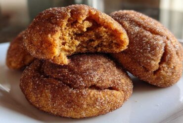 Close-up of three chewy pumpkin snickerdoodle cookies coated in cinnamon sugar, one broken open to show the soft interior.