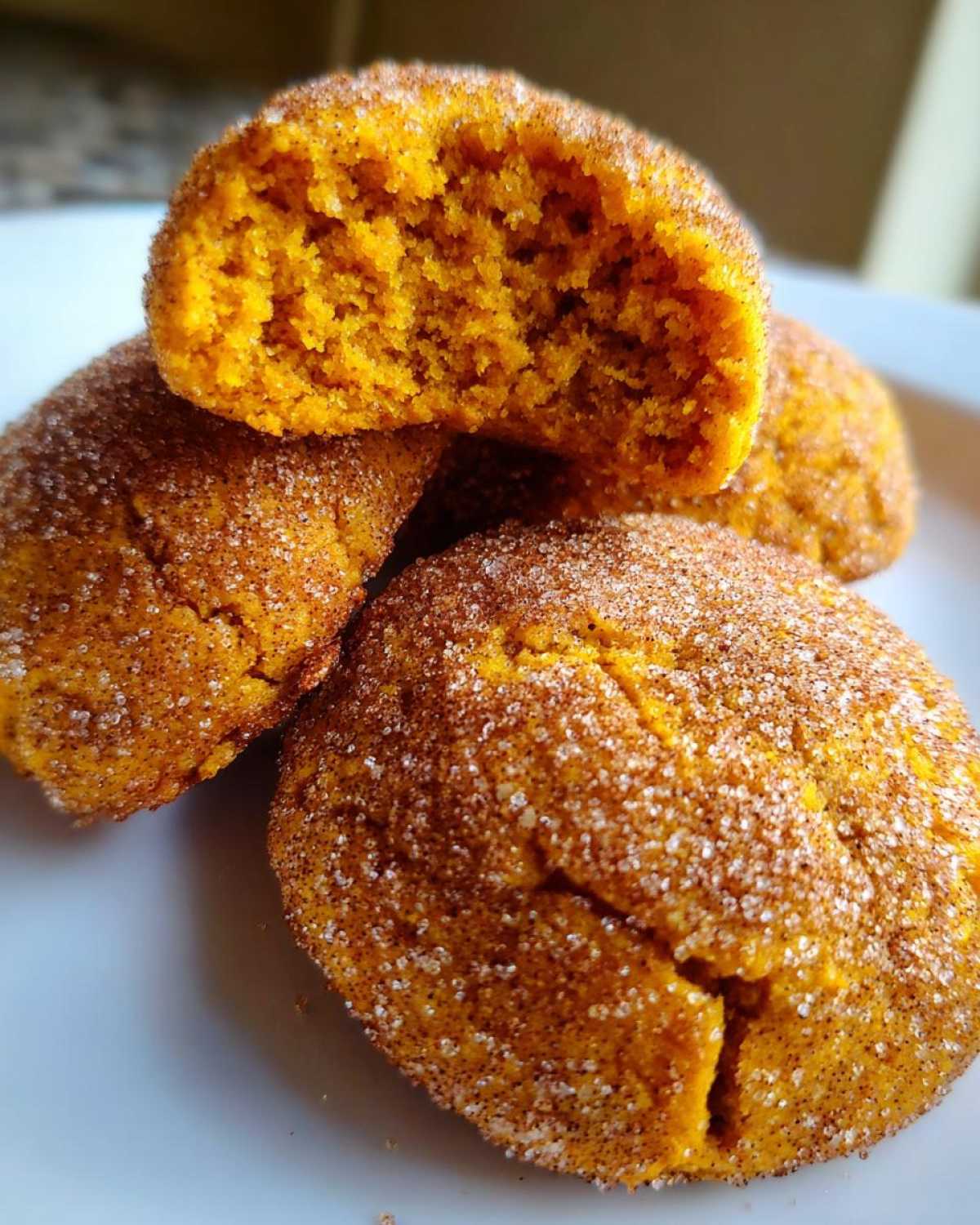 Close-up of chewy pumpkin snickerdoodle cookies coated in cinnamon sugar, one broken open to show the soft interior.