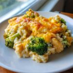 A close-up serving of creamy chicken broccoli rice casserole topped with bubbly, melted cheddar cheese.