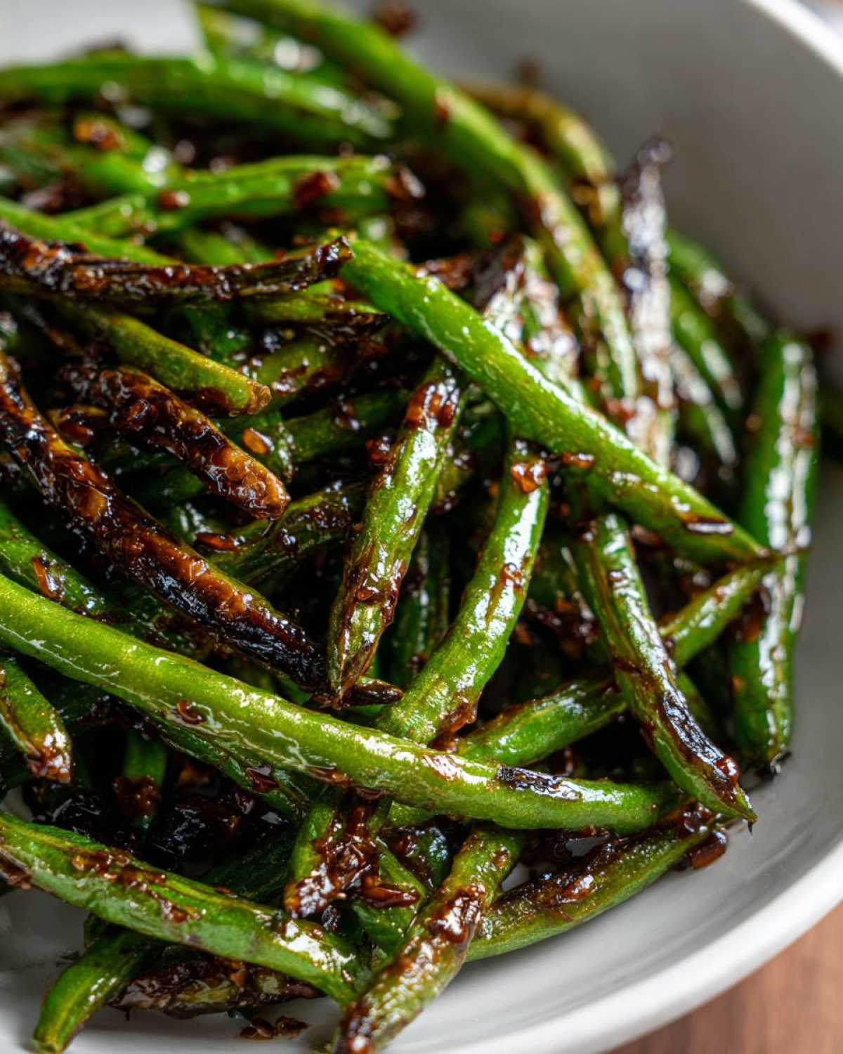Close-up of vibrant green beans coated in a dark, savory garlic sauce, ready to serve.