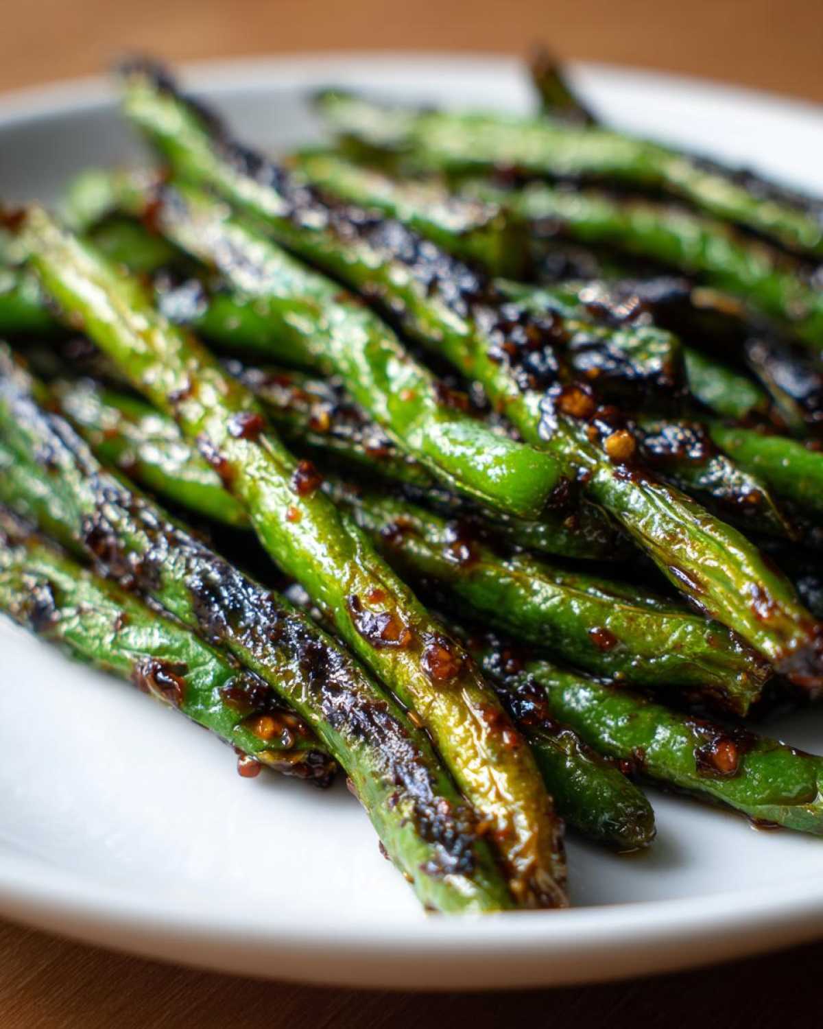 Close-up of vibrant, blistered chinese green beans with garlic sauce served on a white plate.