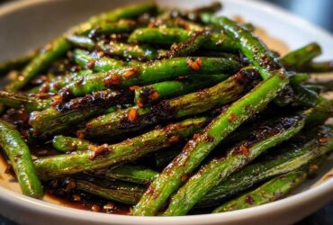 A close-up of vibrant green beans coated in a dark, glossy garlic sauce, ready to serve.