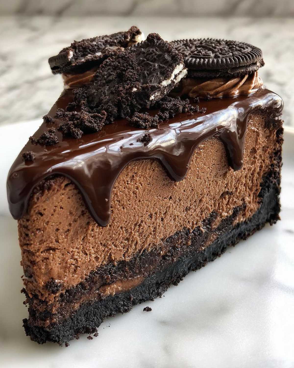 A rich slice of three-layer chocolate cheesecake topped with chocolate ganache, whipped cream, and crushed Oreos.