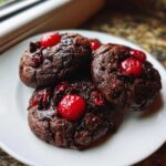 Close-up of three dark, rich chocolate cherry cookies topped with bright red maraschino cherries.