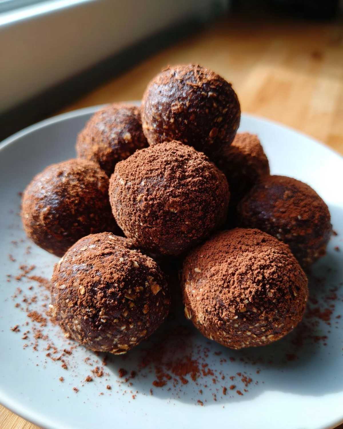 A stack of homemade chocolate protein balls generously dusted with cocoa powder, resting on a light blue plate.