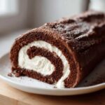 A close-up of a chocolate yule log cake roll showing the dark sponge cake spiraled around a thick white cream filling.