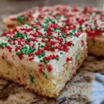 A close-up of a square christmas sugar cookie bars slice topped with thick white frosting and red and green sprinkles.
