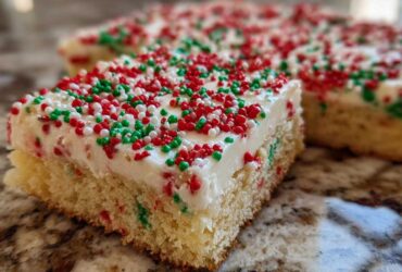 A close-up of a square christmas sugar cookie bars slice topped with thick white frosting and red and green sprinkles.