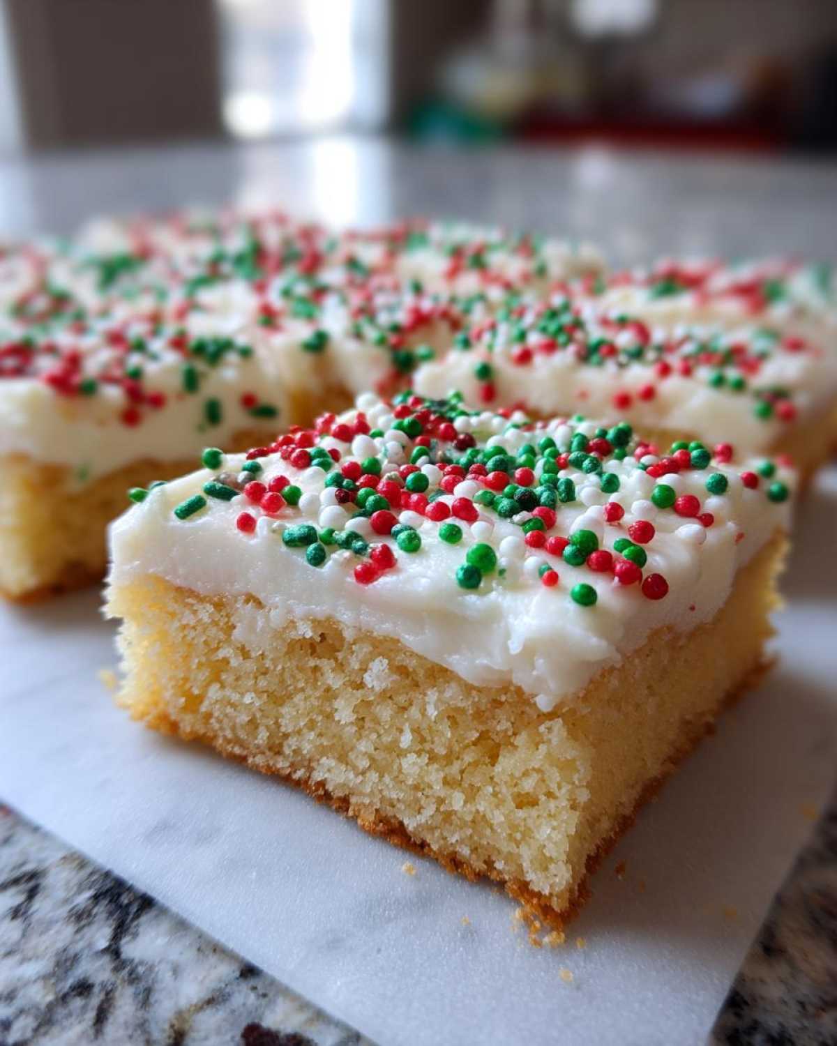 A close-up of a square slice of christmas sugar cookie bars topped with white frosting and red, green, and white sprinkles.