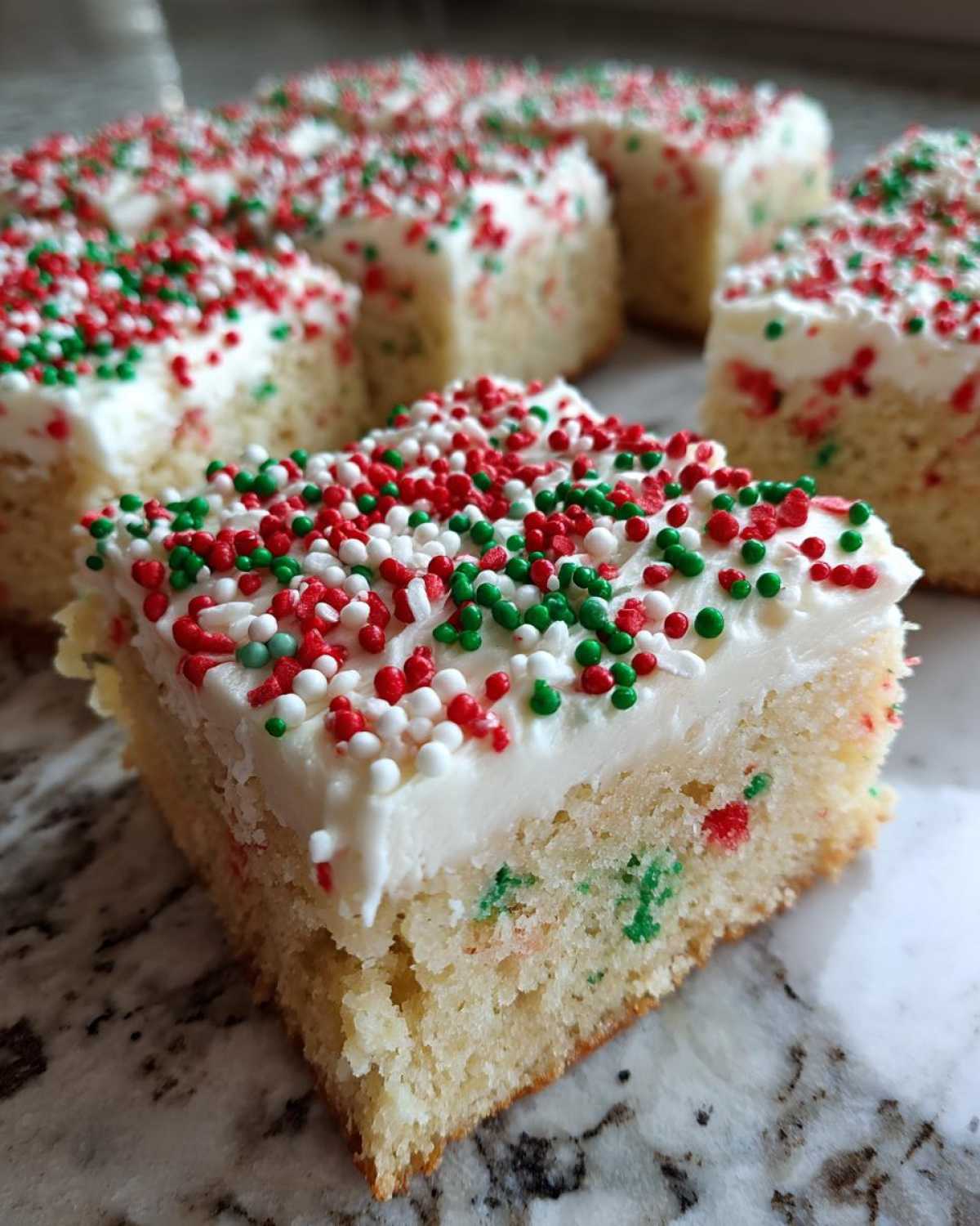 A close-up slice of soft christmas sugar cookie bars topped with thick white frosting and red, green, and white sprinkles.