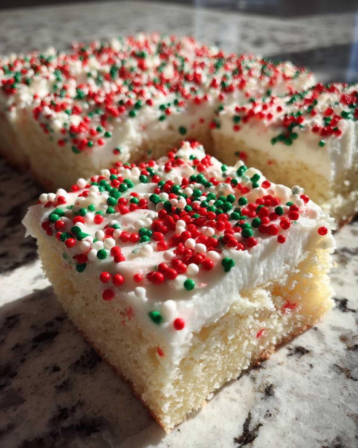 A single square slice of christmas sugar cookie bars topped with thick white frosting and red, green, and white sprinkles.