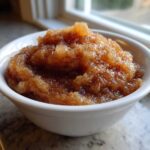 Close-up of chunky, spiced applesauce sprinkled with cinnamon served in a small white bowl.