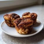 Three golden brown cinnamon sugar french toast muffins served on a small white plate.