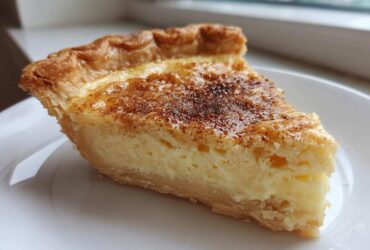A perfect slice of classic custard pie with a golden crust and cinnamon topping on a white plate.