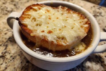 Close-up of a rich, dark french onion soup topped with a crouton and bubbly, melted Gruyère cheese.