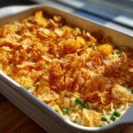 Close-up of a creamy Tuna Casserole topped generously with crunchy, golden cornflakes, showing peas mixed in.