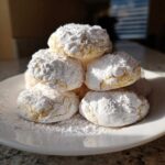 A stack of soft, powdered sugar-dusted cool whip cookies piled high on a white plate.