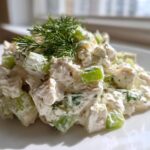 A mound of creamy cottage cheese chicken salad featuring chunks of white meat chicken and bright green celery, topped with fresh dill.