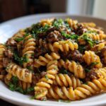 A close-up shot of a bowl of creamy beef pasta made with fusilli noodles and topped with fresh parsley.