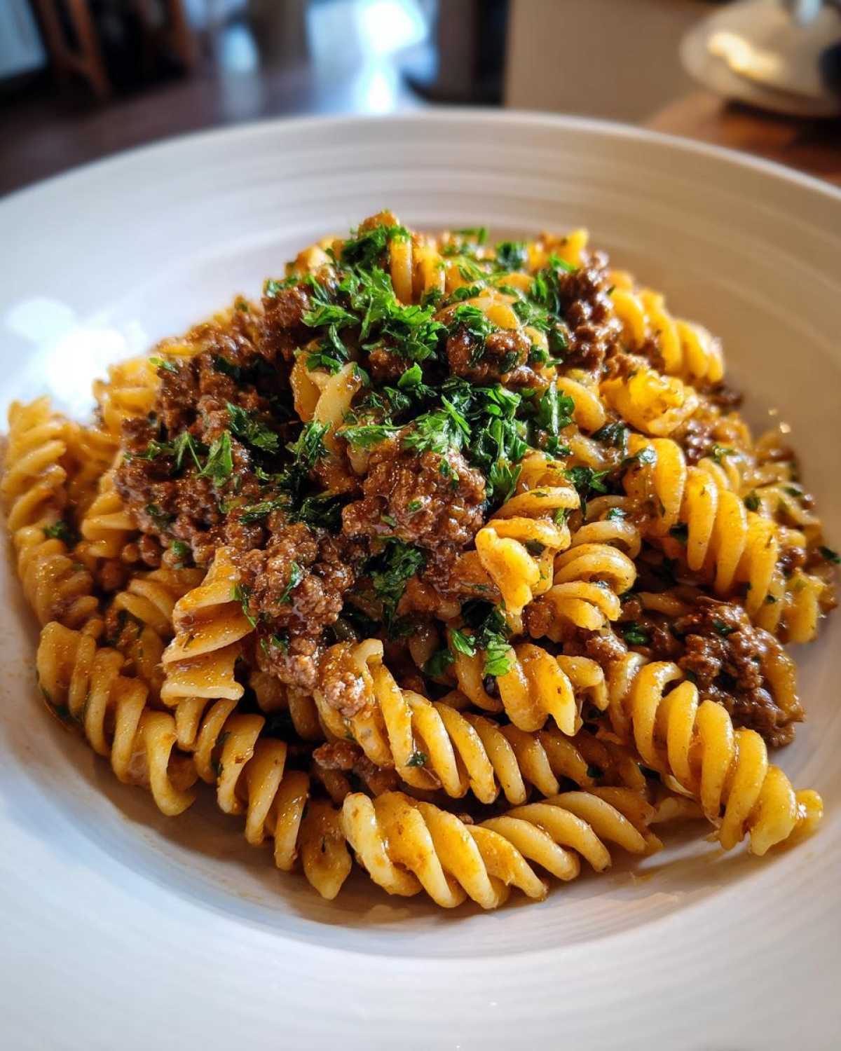 Close-up of creamy beef pasta made with fusilli, topped generously with browned ground beef and fresh chopped parsley.