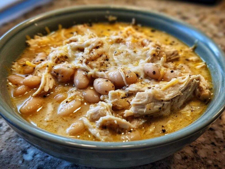 Close-up of a bowl of creamy white chicken chili featuring shredded chicken, white beans, and melted cheese topping.