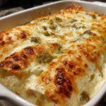 Close-up of baked chicken enchiladas covered in creamy white sauce and melted, bubbly, browned cheese.