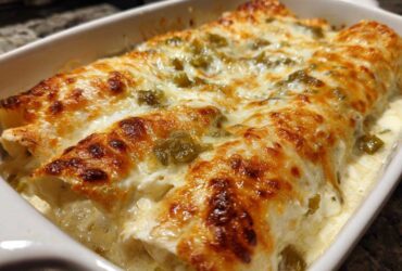 Close-up of baked chicken enchiladas covered in creamy white sauce and melted, bubbly, browned cheese.