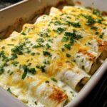 Close-up of baked chicken enchiladas covered in creamy white sauce, melted yellow cheese, and fresh parsley.