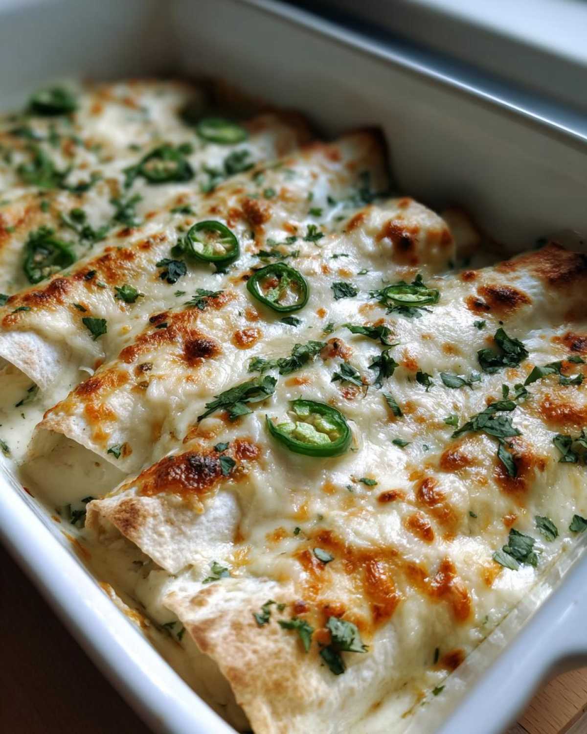 Close-up of baked creamy chicken enchiladas topped with melted cheese, cilantro, and sliced jalapeños.