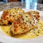 Two pieces of pan-seared creamy lemon chicken covered in a rich, herb-flecked lemon sauce.