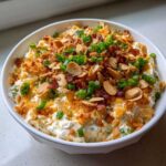 A white bowl filled with creamy Neiman Marcus dip, topped generously with sliced almonds, bacon bits, crispy crumbs, and green onions.