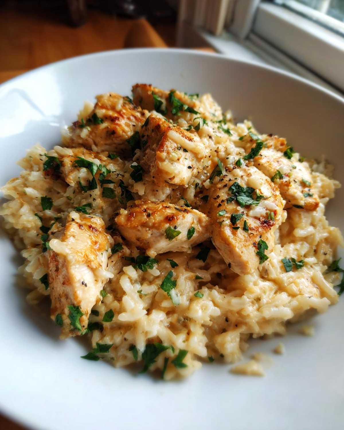 Close-up of a white bowl filled with creamy one pot chicken and rice, topped with browned chicken pieces and fresh parsley.