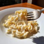 A fork lifting pasta coated in rich, creamy homemade alfredo sauce, showing cheese pull.