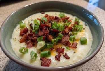 Close-up of a bowl of creamy potato soup recipe topped generously with crispy bacon bits and fresh green onions.