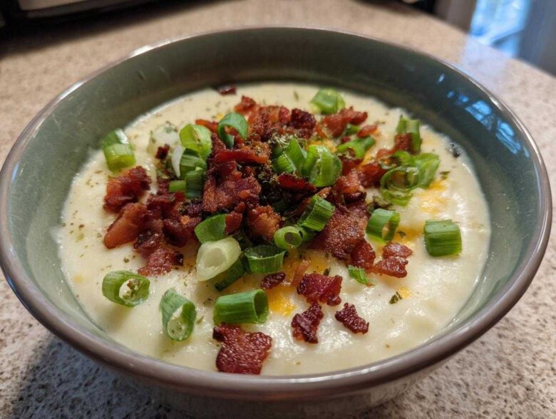 Close-up of a bowl of creamy potato soup recipe topped generously with crispy bacon bits and fresh green onions.