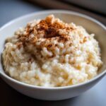 A close-up of creamy rice pudding topped generously with ground cinnamon in a white bowl.