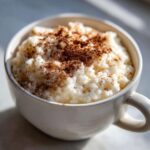 Close-up of creamy rice pudding recipe served in a white mug, generously sprinkled with cinnamon.