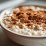 Close-up of a white bowl filled with creamy rice pudding recipe, generously dusted with cinnamon powder.
