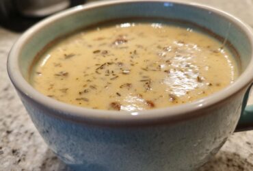 Close-up of creamy sausage potato soup garnished with herbs in a light blue ceramic mug.