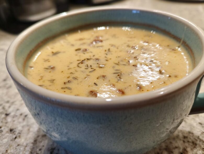 Close-up of creamy sausage potato soup garnished with herbs in a light blue ceramic mug.