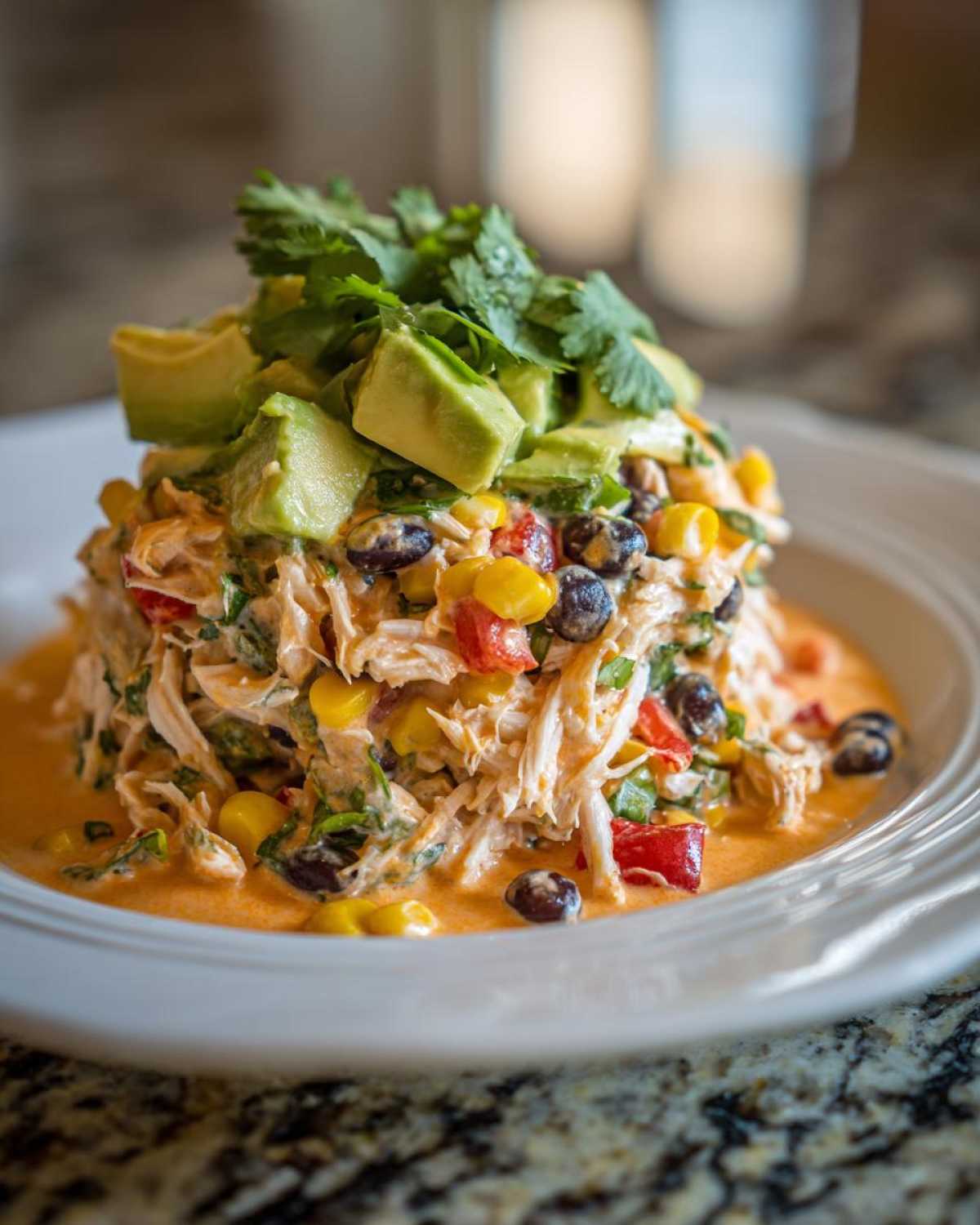 A mound of creamy southwest chicken salad mixed with corn and black beans, topped with avocado and cilantro.