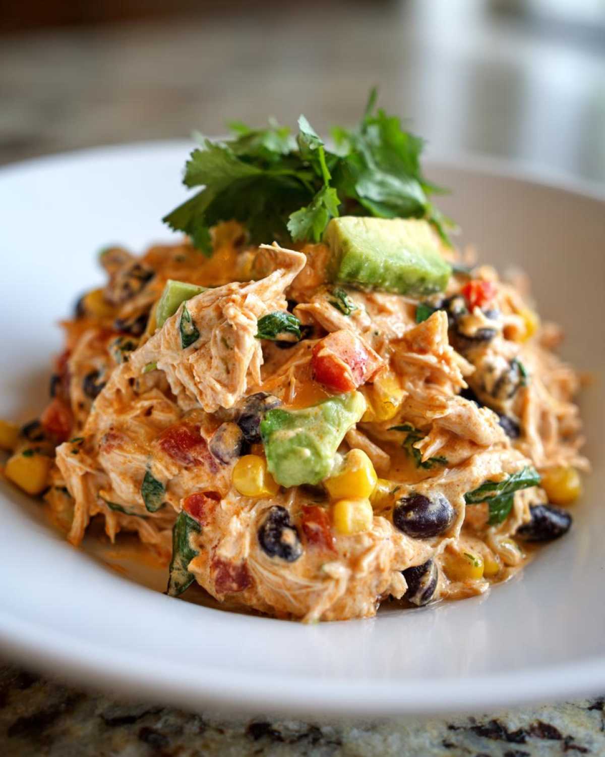 Close-up of creamy southwest chicken salad mixed with black beans, corn, and topped with avocado and cilantro.