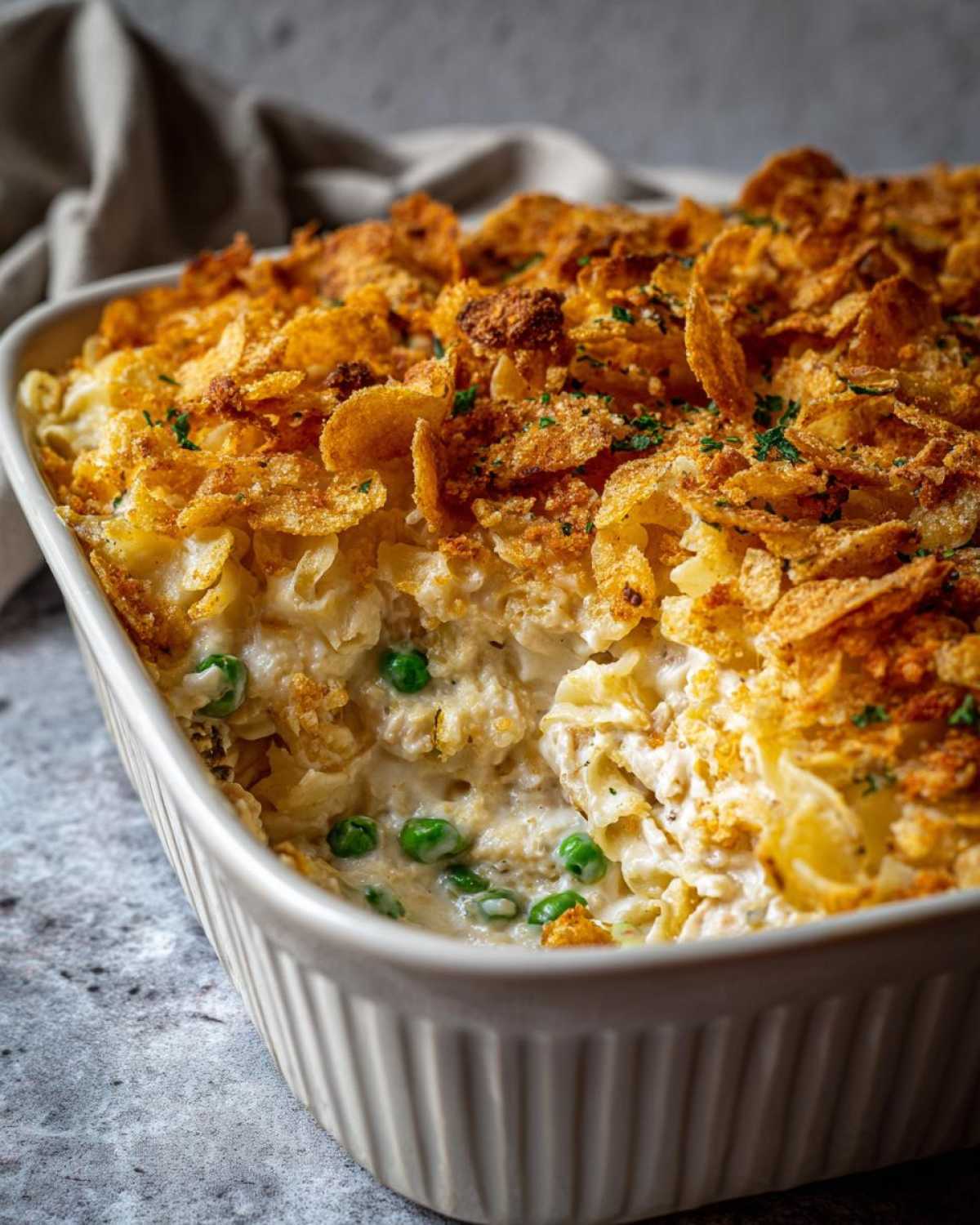 A close-up of a creamy Tuna Casserole in a white baking dish, topped with golden, crunchy cornflakes.