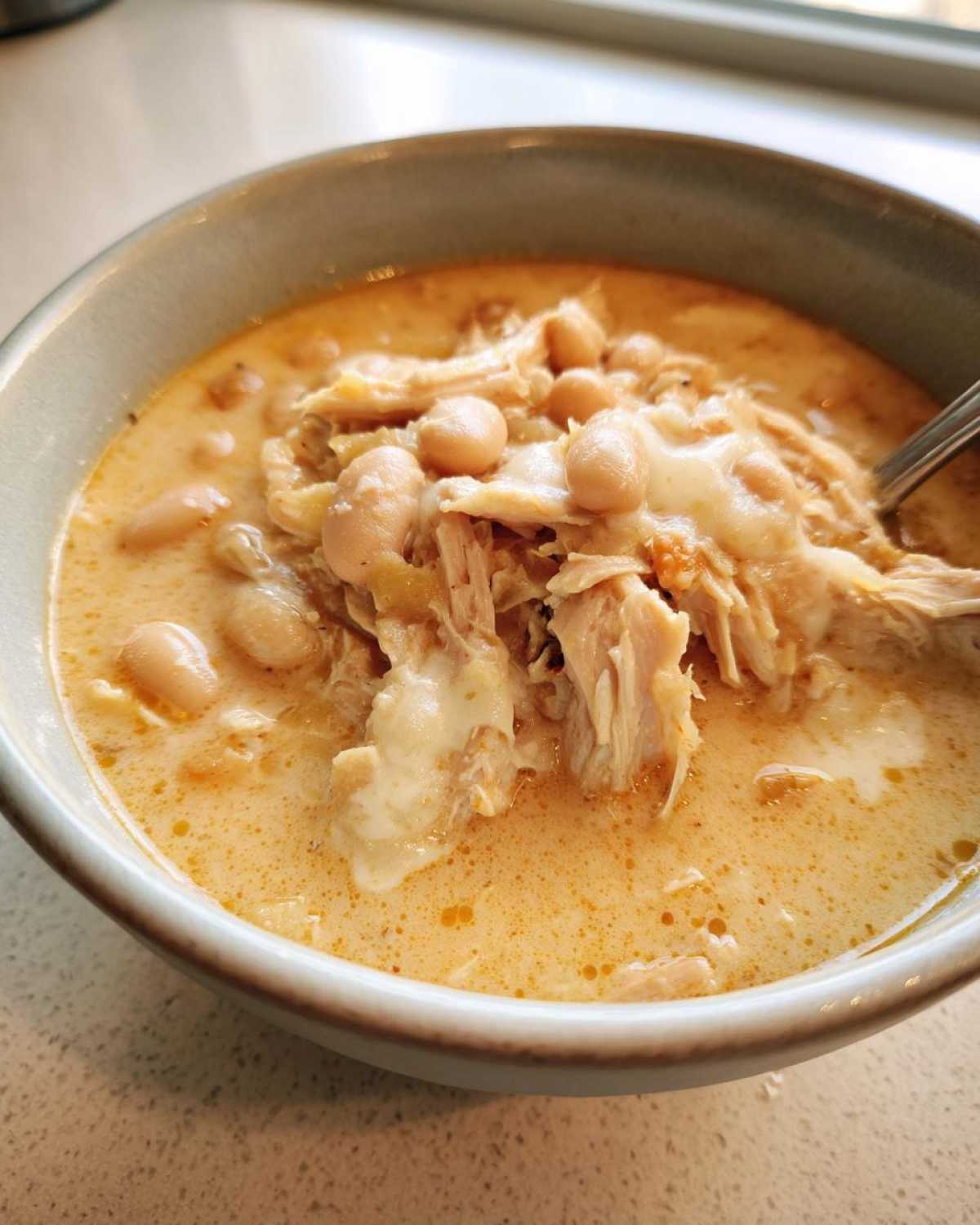 Close-up of creamy white bean chicken chili with shredded chicken and melted cheese in a light blue bowl.