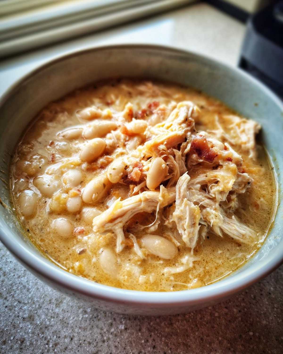 Close-up of a creamy white chicken chili featuring shredded chicken and white beans in a light-colored broth.