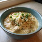 Close-up of a bowl of creamy white chicken chili topped with shredded cheese and fresh parsley.