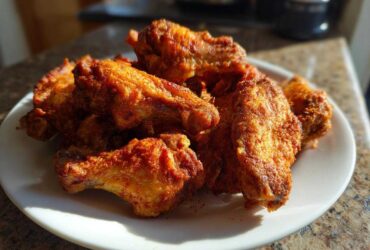 A pile of golden brown, crispy air fryer chicken wings seasoned with spices, served on a white plate.