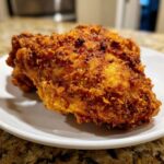 Close-up of a perfectly crispy piece of air fryer fried chicken resting on a white plate.